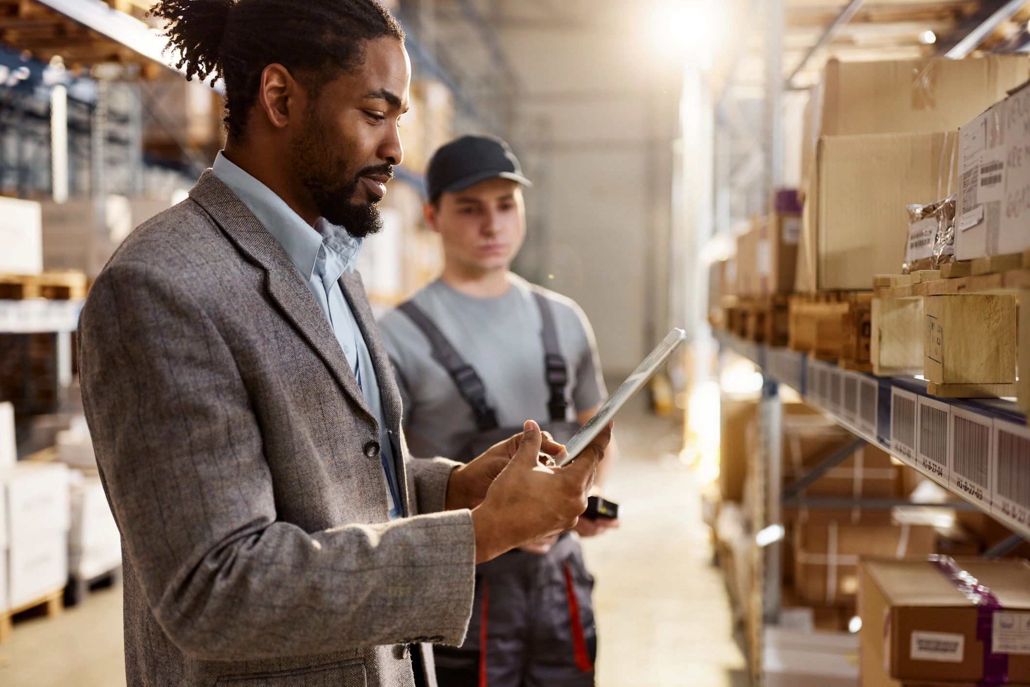 Two African American warehouse coworkers reviewing orders on a tablet